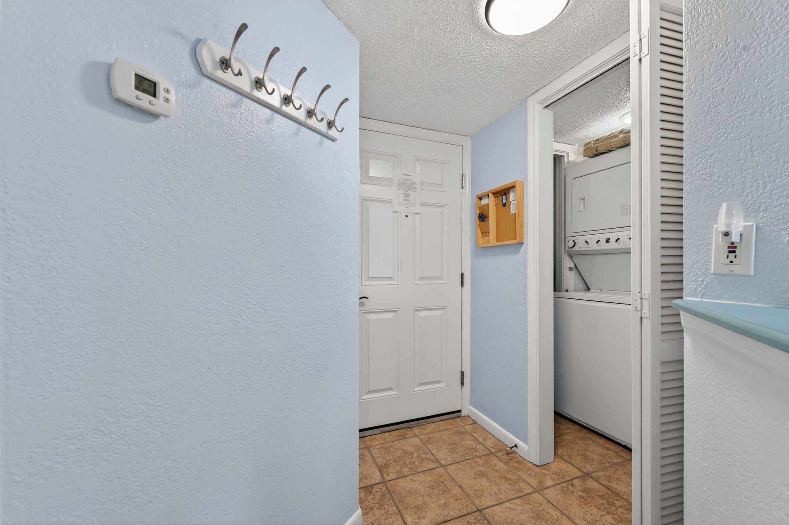 Un couloir avec une porte blanche, un porte-manteau, un thermostat et un appareil à laver le linge.
