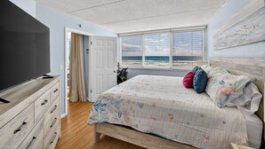 Un dormitorio con cama, televisor, cómoda, puerta y ventana con vistas.