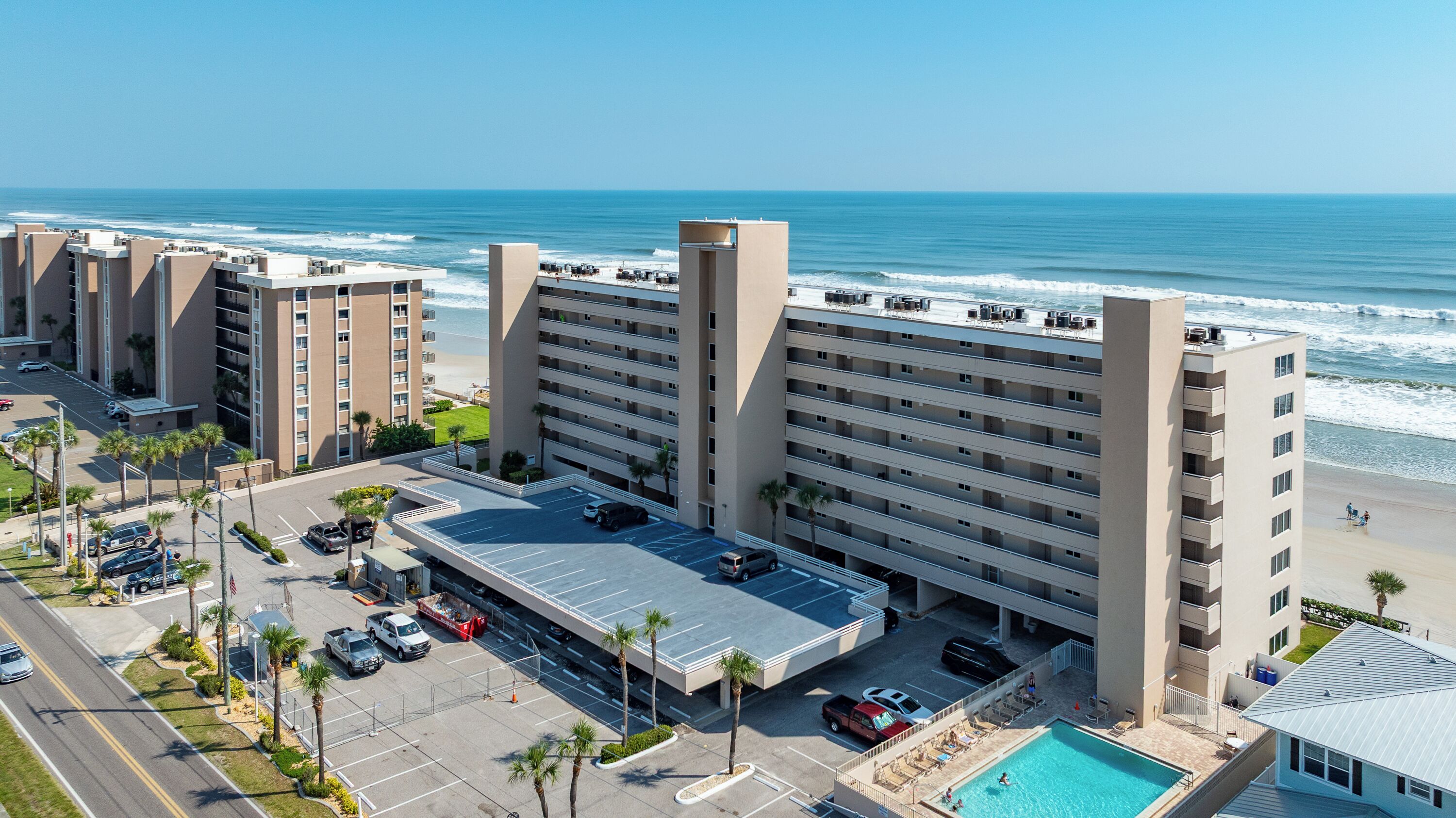 Un hotel moderno con piscina en la azotea, estacionamiento y vistas al océano.