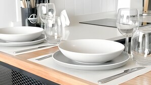 A modern kitchen with white appliances, a dining table set with white plates and bowls, and a water pitcher. - Depto. moderno y acogedor I Wifi I AC (Santiago)