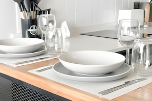Cozinha moderna com eletrodomésticos brancos, uma mesa de jantar posta com pratos e tigelas brancas, e um jarro de água.