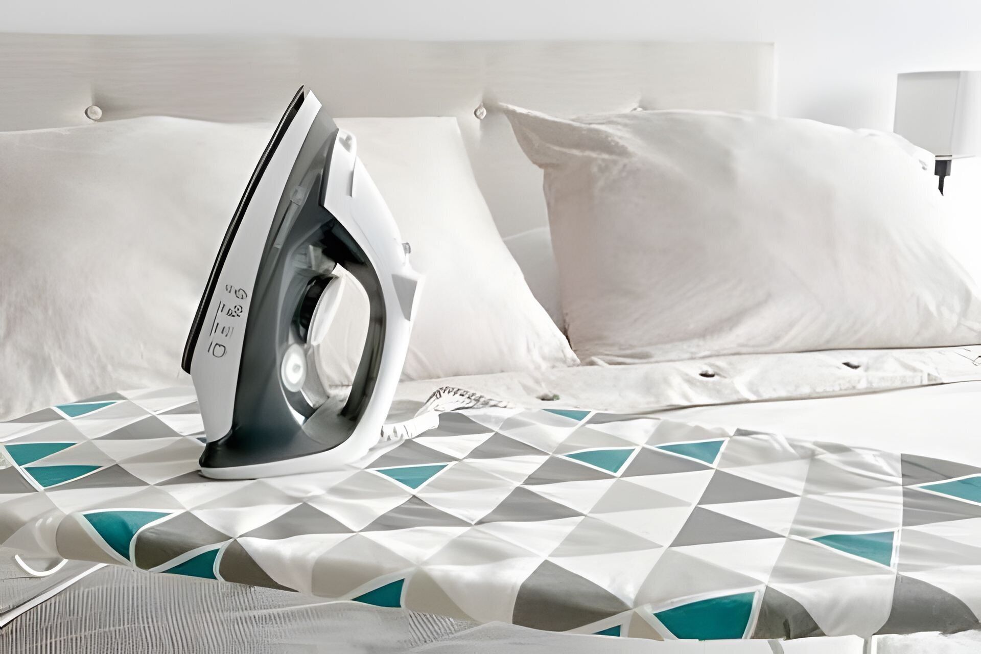 Una cama bien hecha con un edredón estampado con motivos geométricos, un planchador y una almohada.