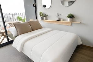Une chambre moderne avec un grand lit, une étagère en bois ornée de plantes et une vue sur le balcon.