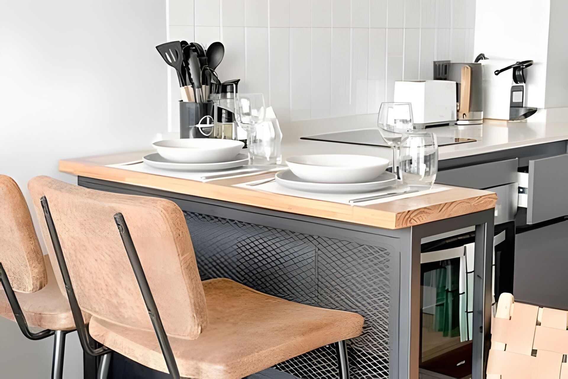A modern kitchen with a dining table set for two, equipped with plates, glasses, and a coffee maker.