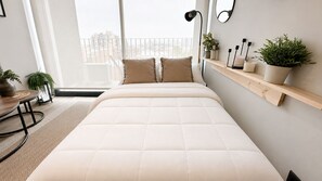 Un dormitorio moderno con una cama grande, una mesita de noche, una silla, una ventana con vistas y una estantería con plantas.