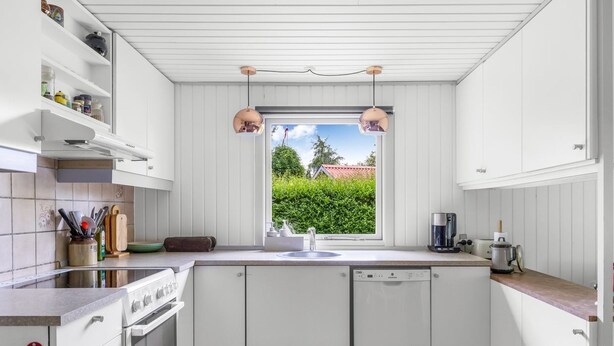 A modern kitchen with white cabinetry, a built-in oven, a dishwasher, and a window with a view of greenery. - "Elif" - 200m from the sea by Interhome (Nordborg)