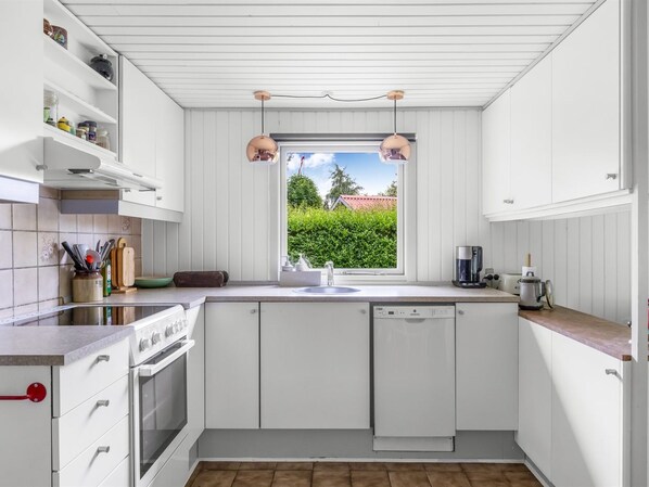 A modern kitchen with white cabinetry, a built-in oven, a dishwasher, and a window with a view of greenery. - "Elif" - 200m from the sea by Interhome (Nordborg)