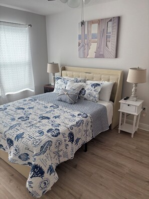 Une chambre à coucher comprenant un lit, deux tables de chevet, une lampe, une fenêtre avec un rideau et une œuvre d’art accrochée au mur.