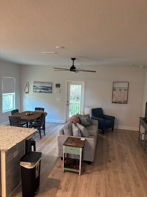 A spacious living area with a dining table, a sofa, a ceiling fan, and a door leading to a balcony. -  Seaglass Sassy’s Beach House Your Santa Rosa Beach Escape (Santa Rosa Beach, Florida)