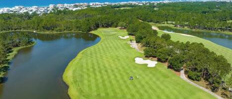 A golf course with water hazards, a clear sky, and a distant view of a coastal town.