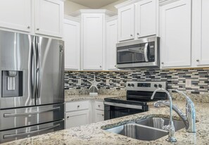 A kitchen with white cabinets, stainless steel appliances, a granite countertop, and a tiled backsplash. -  Seaglass Sassy’s Beach House Your Santa Rosa Beach Escape (Santa Rosa Beach, Florida)