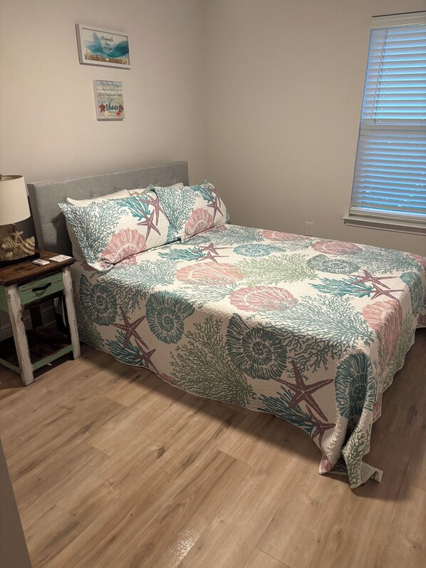 A bedroom with a bed, a nightstand, a lamp, and a window with blinds. -  Seaglass Sassy’s Beach House Your Santa Rosa Beach Escape (Santa Rosa Beach, Florida)