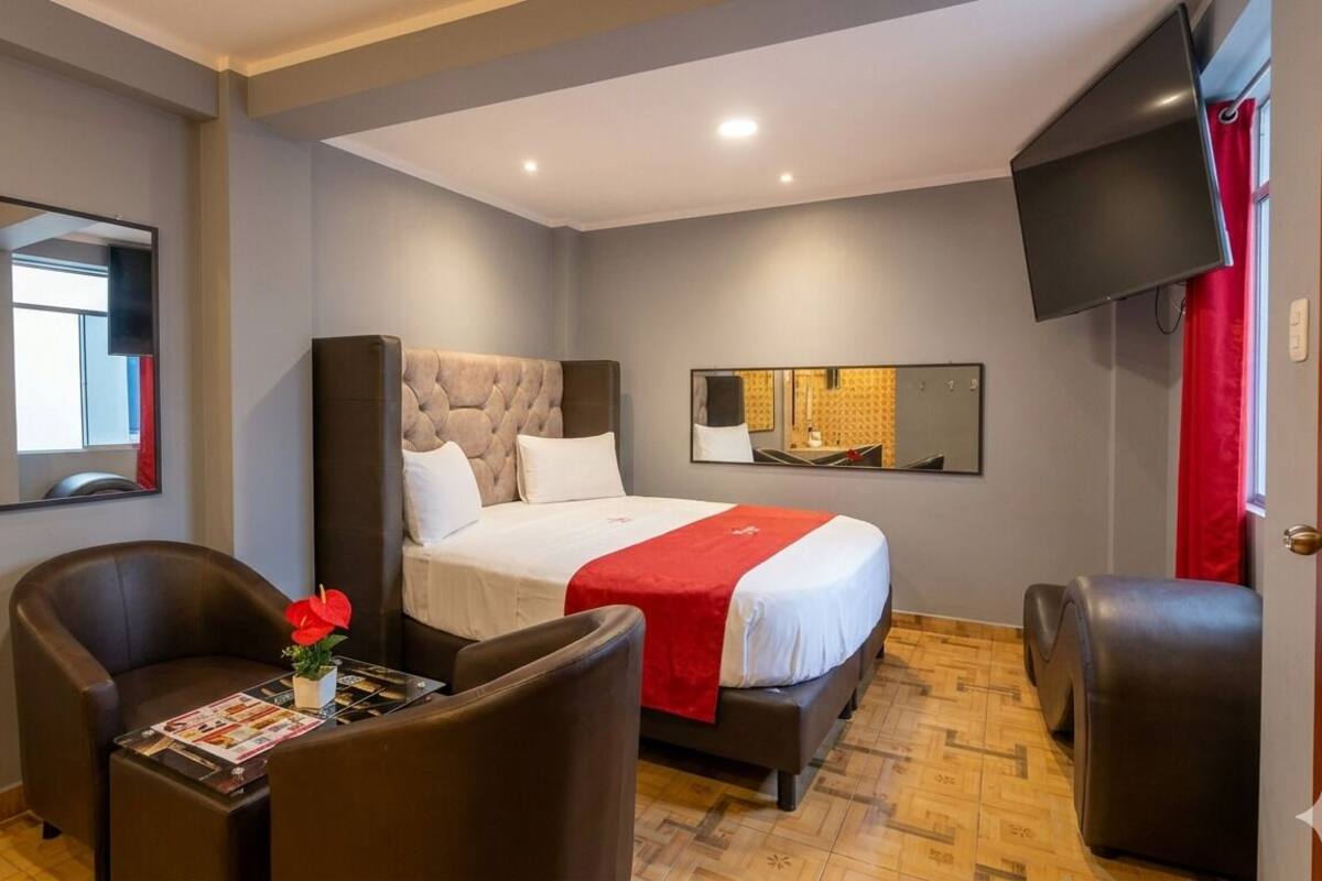 A hotel room with a bed, a desk with a chair, a TV, and a mirror.