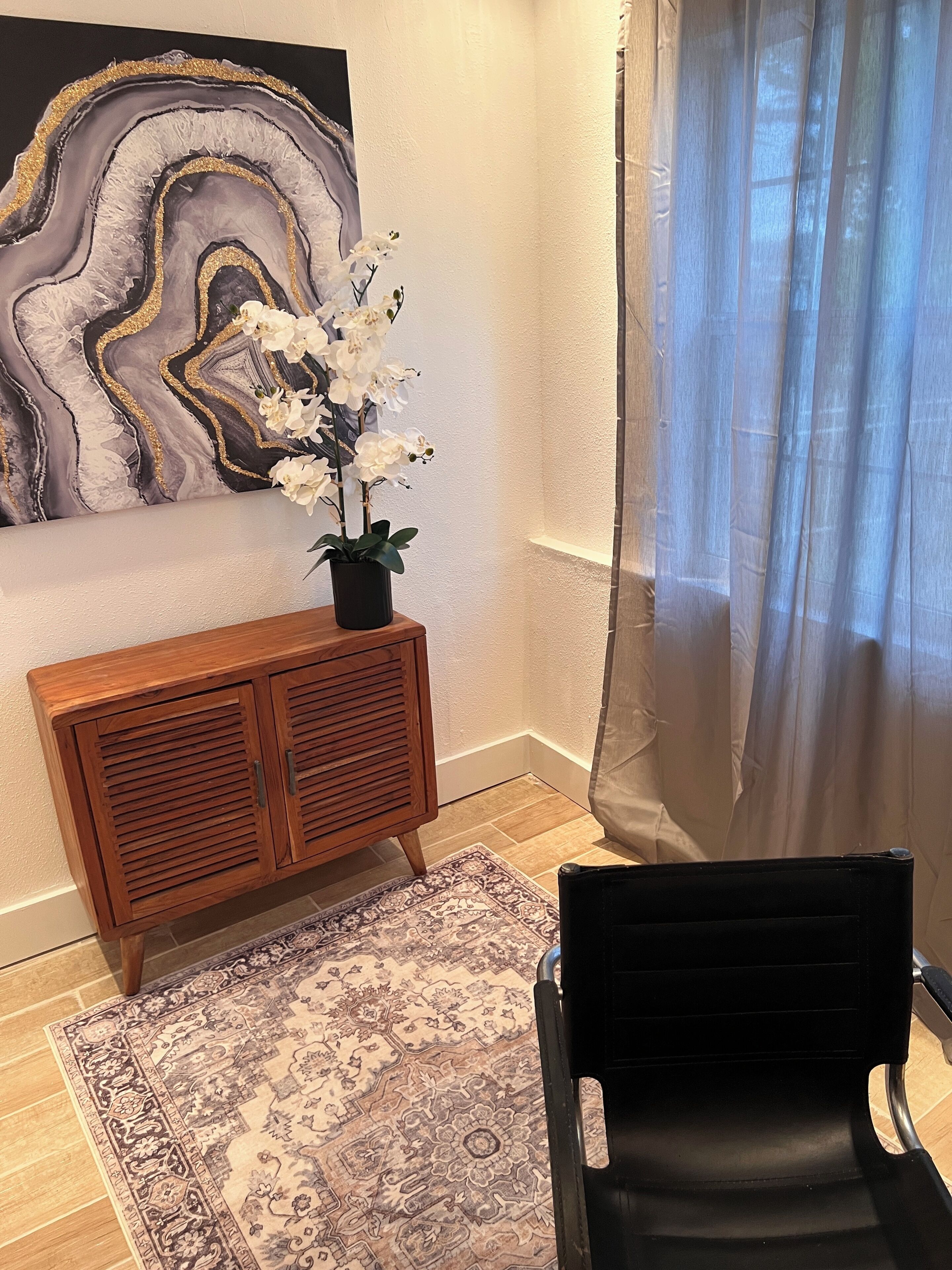 Ein Zimmer mit einem Holzkasten, einem gemusterten Teppich, einem schwarzen Stuhl und einem Gemälde an der Wand.