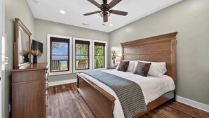 Un dormitorio con cama, ventilador de techo, cómoda, televisor y ventana con vistas.