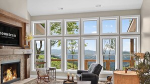 Amplia sala de estar con chimenea, ventanas grandes, un área de estar acogedora y vistas al exterior.