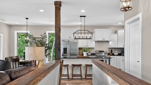 Una cocina moderna con armarios blancos, una isla de madera y un comedor con banco y taburetes.