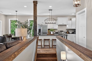 Una cocina moderna con armarios blancos, una isla de madera y un comedor con banco y taburetes.