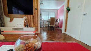 A modern living room with a TV, wooden decor, a dining area, and a red rug. - Lovely Clydebank Apartment - 2 Bedrooms (Clydebank)