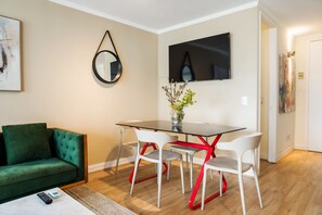 Una sala de estar moderna con un sofá verde, una mesa de comedor con cubierta de vidrio y detalles rojos, y un televisor de pantalla plana montado en la pared.