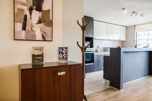 A modern kitchen with white cabinets, a wooden cabinet with a picture frame, and a wooden coat rack. - Luxury 2 Bedroom Apartment with Pool and Parking (Las Condes)