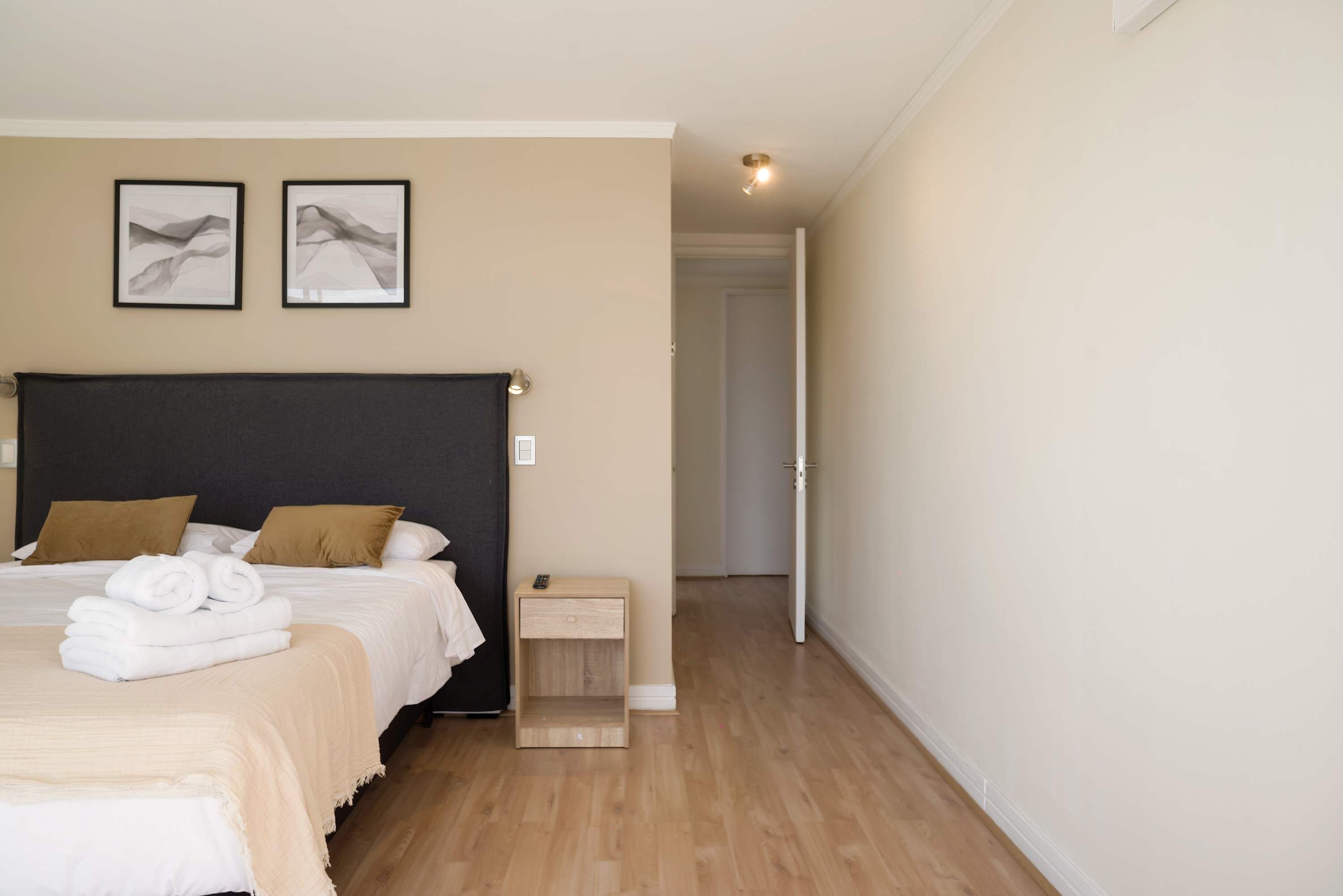 A bedroom with a large bed, a bedside table, and two framed pictures on the wall.