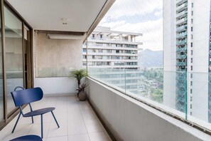 A balcony with a chair, a potted plant, and a view of a cityscape and mountains. - Luxury 2 Bedroom Apartment with Pool and Parking (Las Condes)