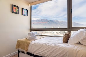A hotel room with a bed, a window with a mountain view, and two framed pictures on the wall. - Las Condes Modern Apartment 2BR2BA, Pool & Views (Las Condes)