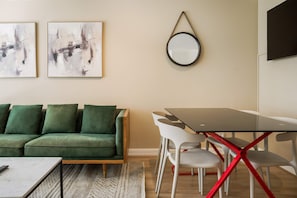 Een kamer met een groene bank, een eettafel met stoelen en twee abstracte schilderijen aan de muur.