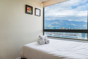 A hotel room with a bed, a window with a mountain view, and two framed pictures on the wall. - Luxury 2 Bedroom Apartment with Pool and Parking (Las Condes)