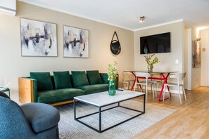 A modern living room with a green sofa, a coffee table, a TV, and abstract art on the wall. - Luxury 2 Bedroom Apartment with Pool and Parking (Las Condes)