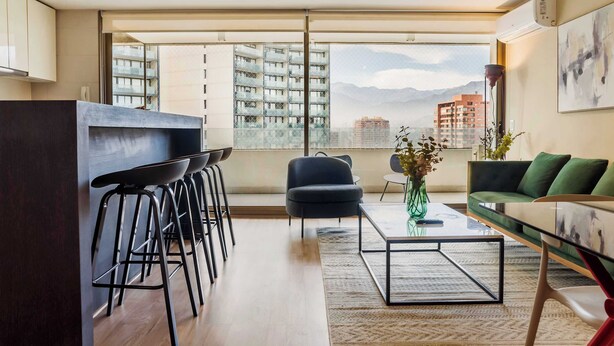 Ein modernes Wohnzimmer mit Küchenbereich, großen Fenstern und Blick auf Gebäude und Berge.