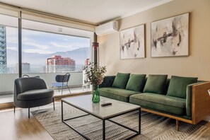Een moderne woonkamer met een groene bank, een zwarte fauteuil, een salontafel en een vaas met bloemen.