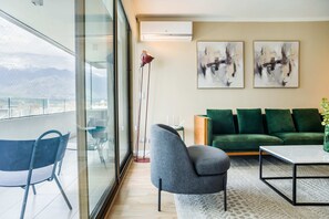 Ein modernes Wohnzimmer mit einem grünen Sofa, einem grauen Sessel und einem Tisch. An der Wand hängen abstrakte Gemälde und es steht eine Stehlampe dort.