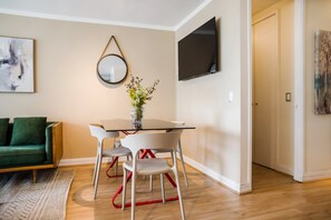 Ein modernes Wohnzimmer mit einem Glastisch, weißen Stühlen, einem grünen Sofa, einem Flachbildfernseher und einem Spiegel an der Wand.