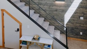 Una escalera con paneles de madera, barandilla de vidrio y una pequeña mesa con libros.