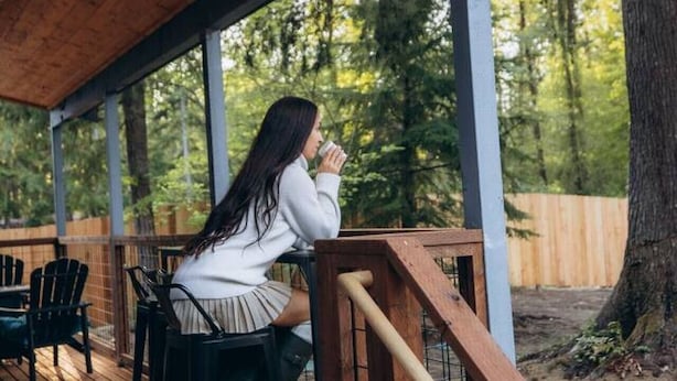 Una terraza de madera con asientos al aire libre, barandilla y vistas a una zona boscosa.