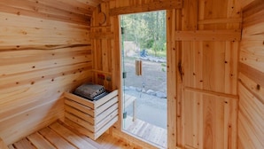 Una sauna de madera con un banco, un banco con una toalla y una puerta que da al exterior.