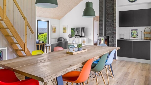 Une cuisine moderne avec une table en bois, des chaises colorées, une cheminée en briques noires et une grande fenêtre.