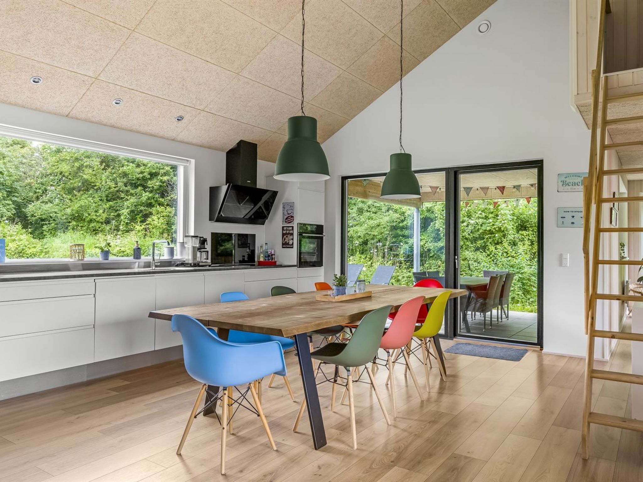 Una cucina moderna con una grande isola, sedie colorate e vista sul verde circostante.