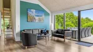 Un salon moderne doté d’une grande fenêtre, d’un canapé en cuir noir, d’une table basse et d’un tableau représentant une scène de plage.