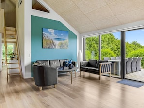 Ein modernes Wohnzimmer mit großem Fenster, einer schwarzen Ledersofa, einem Couchtisch und einem Gemälde, das eine Strandansicht zeigt.