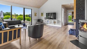 Un vaste espace de vie doté d’une cheminée, d’un téléviseur et d’une grande fenêtre donnant sur un paysage verdoyant.