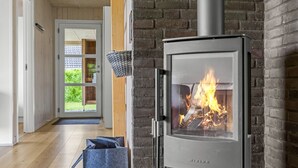 Un intérieur moderne agrémenté d’un poêle à bois, d’un panier mural et d’une porte donnant sur un espace extérieur verdoyant.