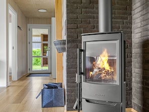 Ein modernes Interieur mit Kaminofen, einem Korb an der Wand und einer Tür zu einem grünen Außenbereich.