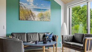 Un salon moderne avec un canapé, une table basse ronde et une grande fenêtre donnant sur un paysage verdoyant et une plage.