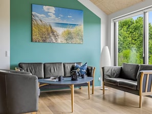 Ein modernes Wohnzimmer mit einer Couch, einem runden Couchtisch und einem großen Fenster mit Blick auf Grünflächen und einen Strand.