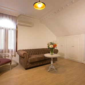 A room with a brown sofa, a round table with a vase of flowers, a chair, and a wardrobe. - La Villa Blanche Hotel (Istanbul)