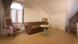 Una habitación con un sofá marrón, una silla, una mesita redonda con un florero y un armario blanco.