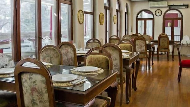 Un comedor con mesas y sillas de madera, ventanas grandes y un reloj en la pared.